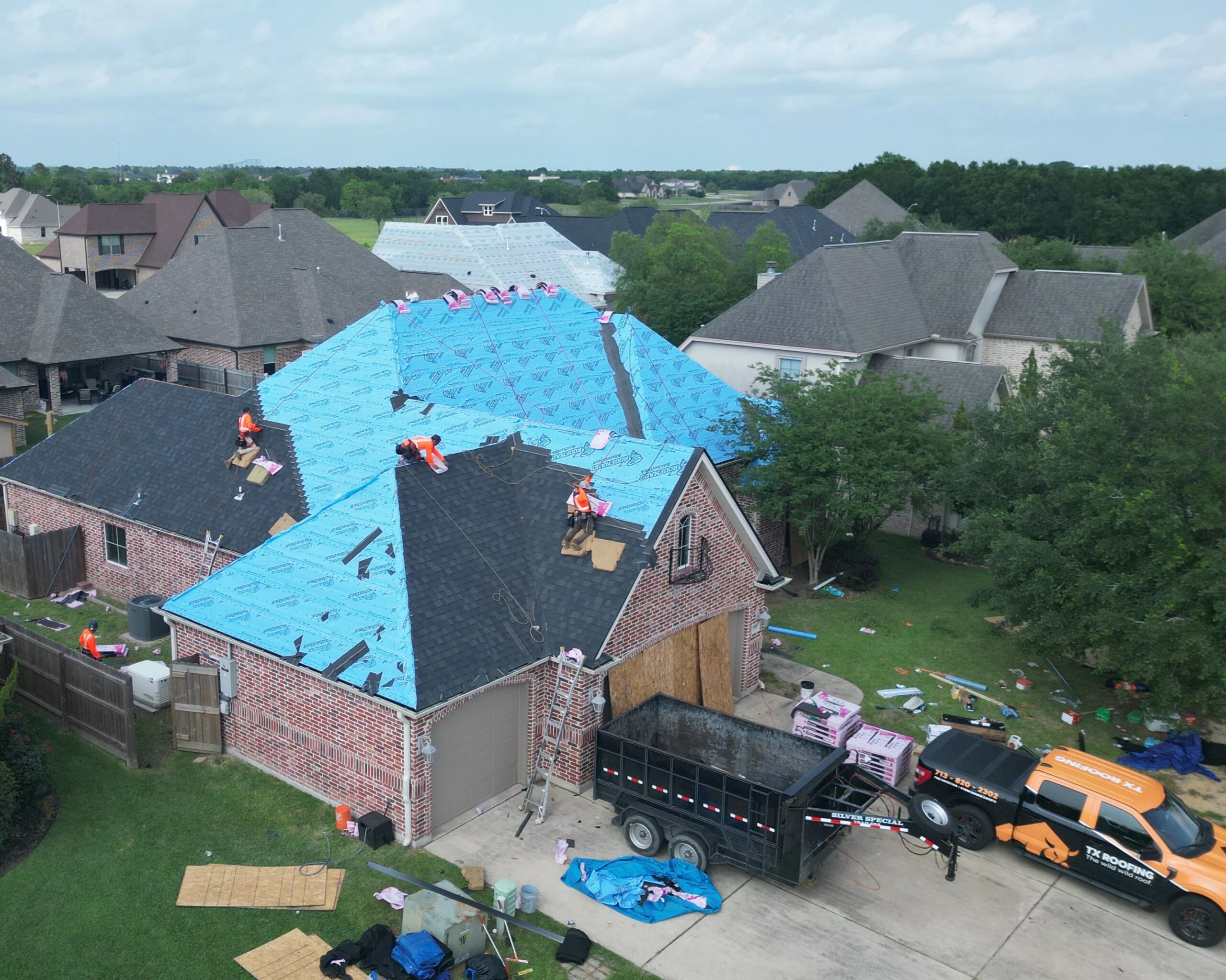Aerial view of a residential roof replacement project with professional roofers installing new underlayment and asphalt shingles.