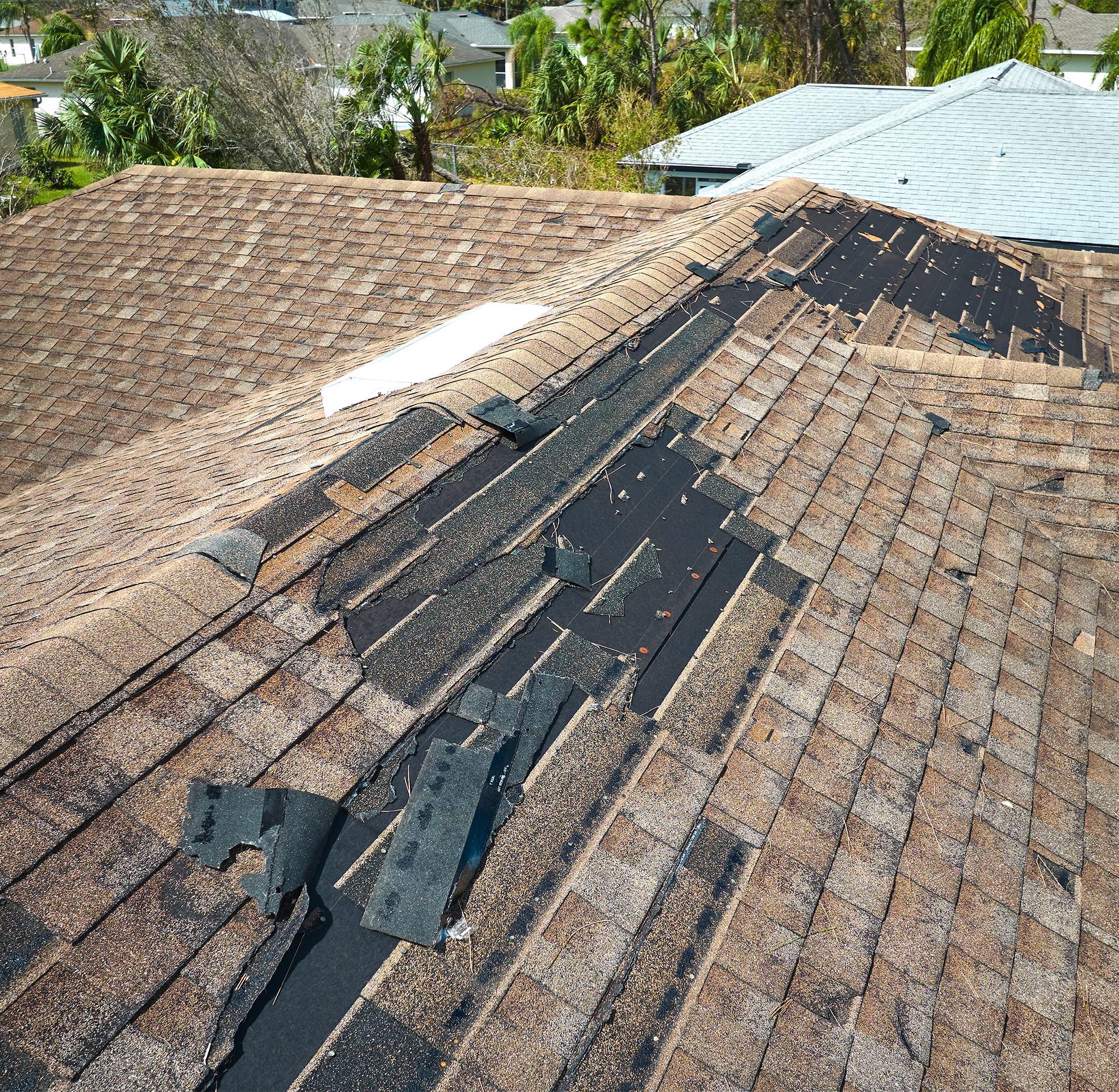 Storm-damaged asphalt shingle roof with missing ridge shingles and exposed underlayment requiring professional repair or replacement.