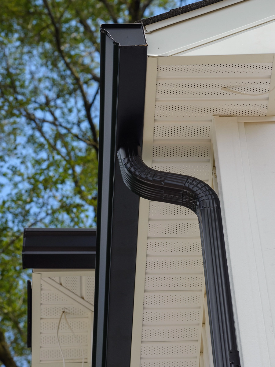Black seamless gutter and downspout system installed on a residential home for effective rainwater drainage.