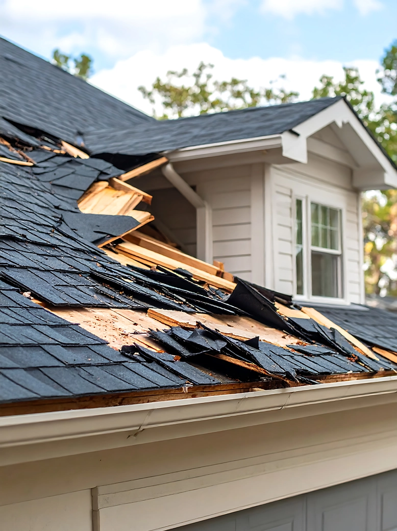 Severe storm damage to a residential roof with torn shingles, exposed decking, and structural damage requiring immediate repair.