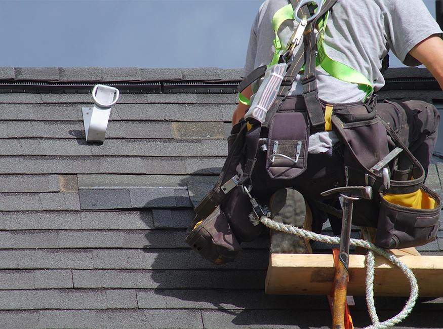 Professional roofing contractor installing architectural shingles on a residential roof using industry-standard safety equipment.