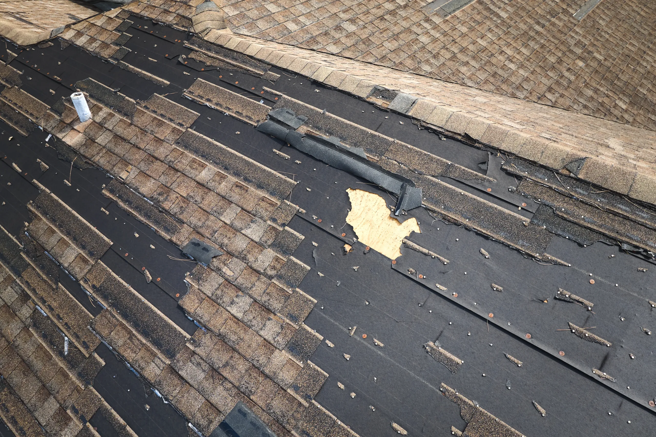 Storm-damaged asphalt shingle roof with significant shingle loss and exposed underlayment requiring professional repair or replacement.