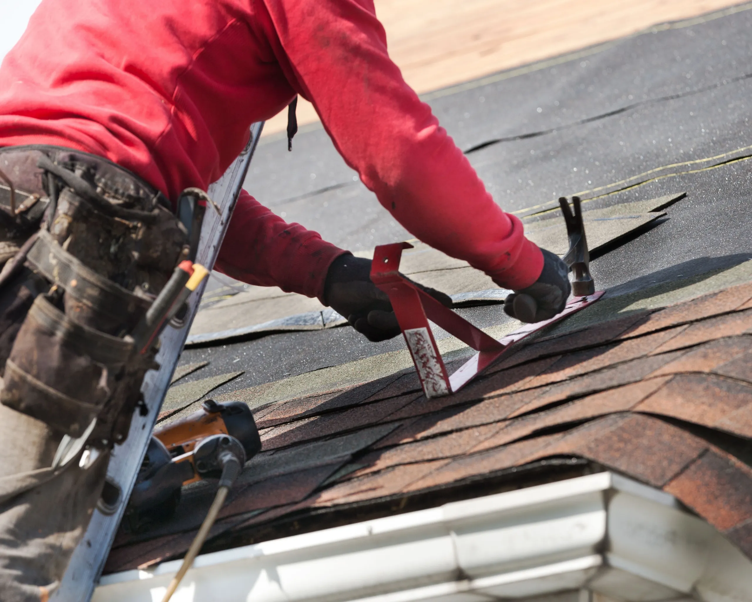 Professional roofing contractor repairing and installing asphalt shingles on a residential roof.